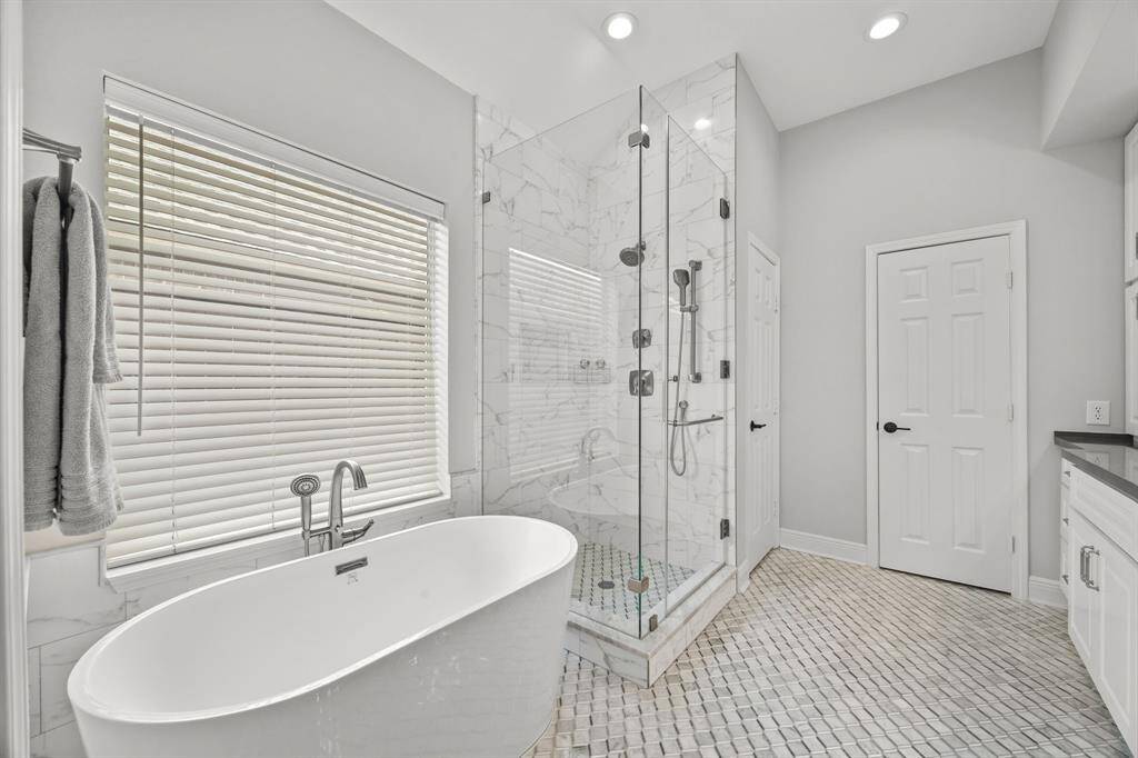 Unwind in this elegant primary bathroom featuring updated tile flooring and a soothing soaker tub, perfect for relaxation.