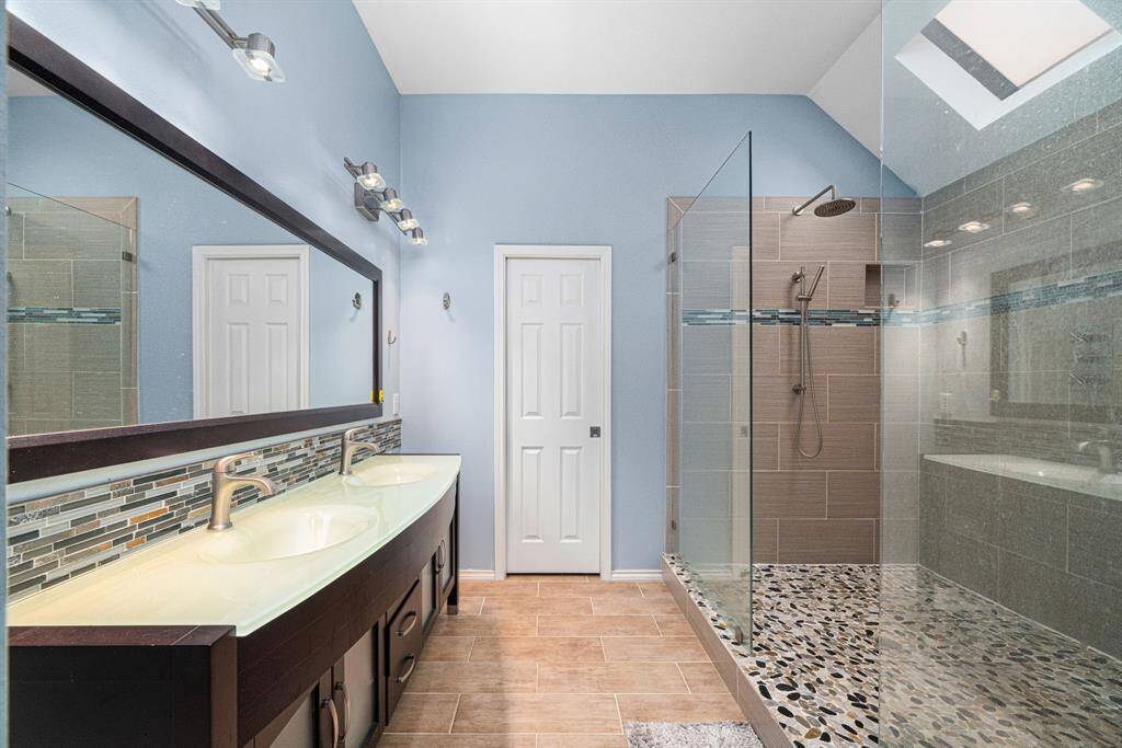 Spa-Inspired Primary Bathroom. Indulge in this expansive ensuite bathroom, designed like a high-end spa retreat. The oversized walk-in shower features dual showerheads for a lavish experience, while two custom skylights bathe the space in warm, natural light. A sleek double-sink vanity provides ample space for getting ready, complemented by modern lighting fixtures that add a touch of elegance. Stylish tilework flows throughout, creating a cohesive, contemporary