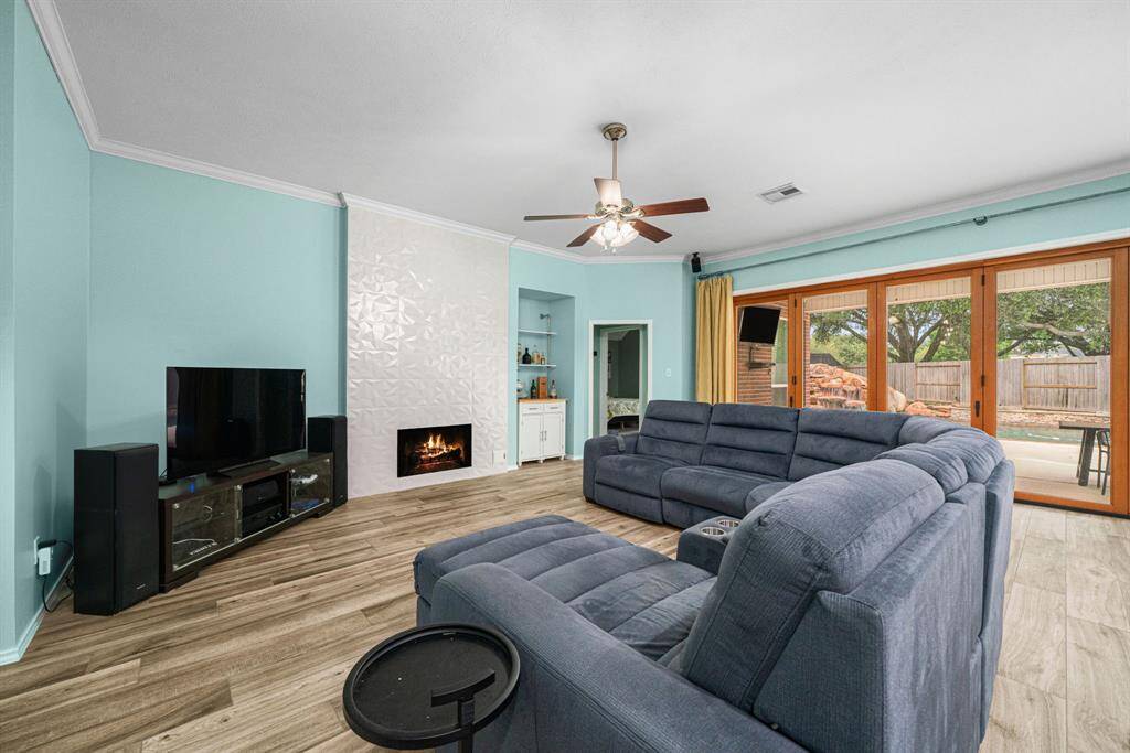 Bask in this spacious living room, where soaring ceilings adorned with elegant crown molding create an atmosphere of refined luxury. The focal point is a stylish modern gas fireplace, surrounded by custom built-in shelving. Expansive accordion doors disappear to merge your indoor sanctuary with the covered patio oasis, creating the ultimate entertainment space for both intimate gatherings and grand celebrations. Sleek ceramic tile flooring flows seamlessly throughout the common areas.