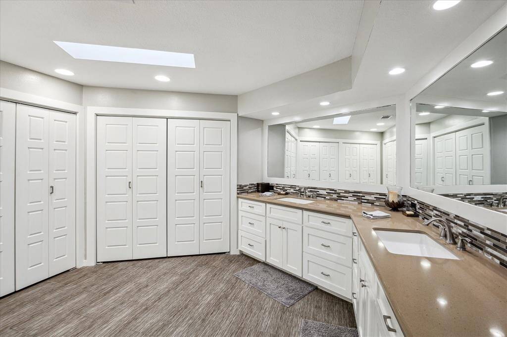 This spacious bathroom features dual sinks with ample counter space, modern cabinetry, and a large mirror. The room is well-lit with recessed lighting and a skylight, complemented by stylish tile flooring and plenty of closet storage.