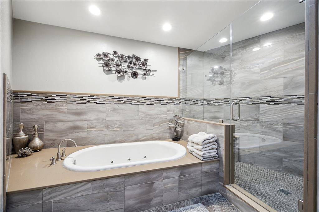 This modern bathroom features a spacious glass-enclosed shower and a luxurious built-in bathtub, accented with elegant tile work and stylish decor.