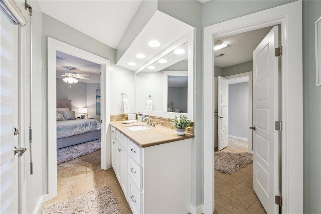 This photo showcases a modern bathroom with a sleek vanity, ample lighting, and a large mirror. It connects directly to two bedrooms.