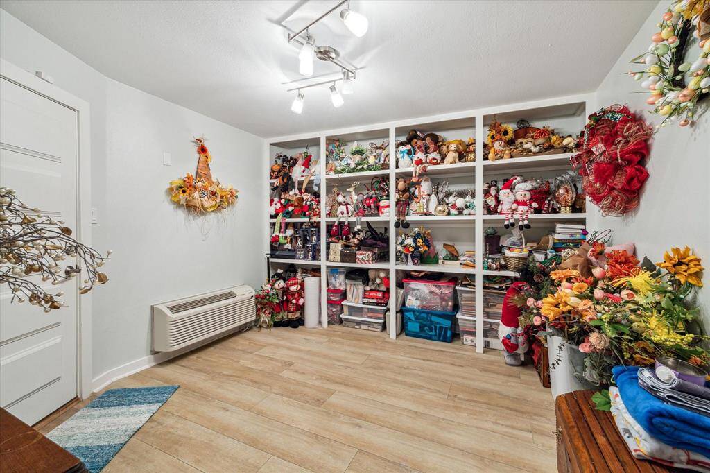 This extra storage room off the fourth bedroom/office features built-in shelves perfect for decorative items and holiday decor. It has wood-like flooring, bright overhead lighting, and a wall-mounted air unit, perfect for organizing and seasonal storage.