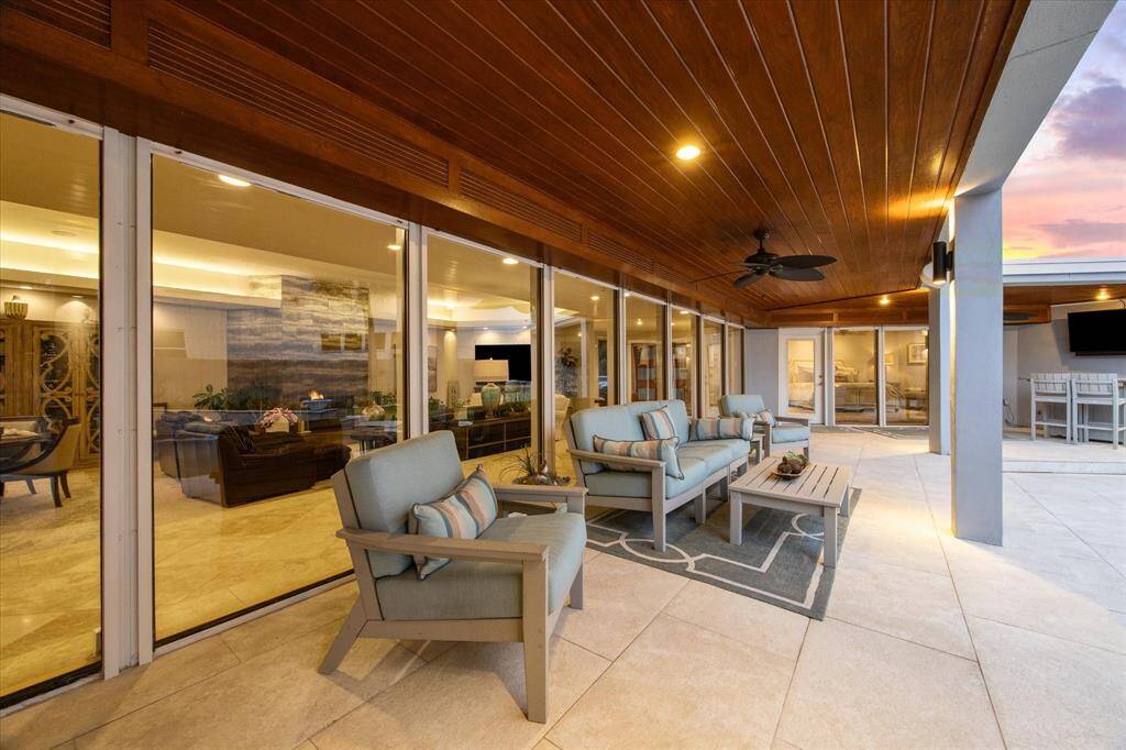 This photo showcases a spacious outdoor patio with comfortable seating, modern ceiling fans, and a warm wood-paneled ceiling. Large glass doors provide seamless indoor-outdoor living, leading to an inviting interior space. Perfect for relaxing and entertaining.