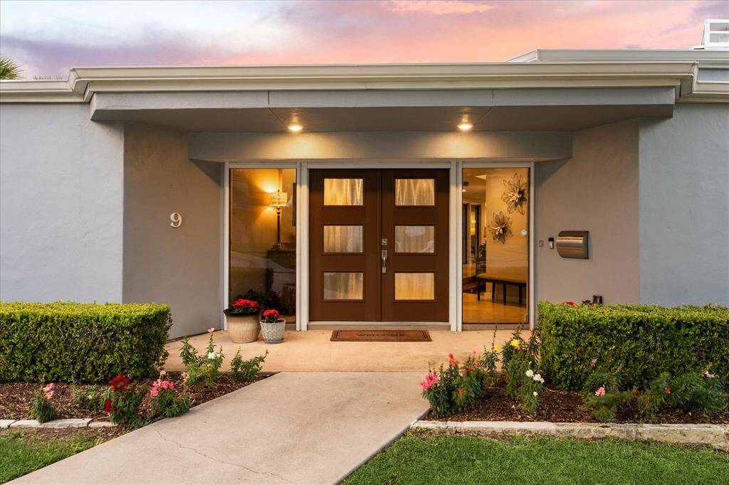 This photo showcases a modern, welcoming entrance with a double door, flanked by large windows, as well as well trimmed hedge and landscaped front.