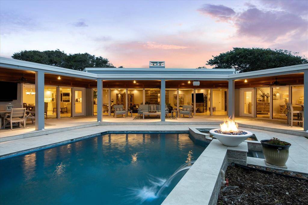 This is another photo of the spacious backyard featuring a swimming pool and a fire pit. The open layout includes a covered patio with outdoor seating and ample lighting, perfect for entertaining. Large glass doors connect the indoor and outdoor spaces, creating a seamless flow.