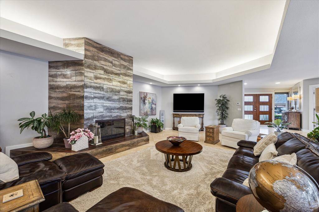 This spacious living room features a modern design with a large, stylish fireplace as the focal point. It includes plush seating, a mounted flat-screen TV, and elegant lighting. Natural light streams in through large windows, enhancing the inviting atmosphere. Perfect for entertaining or relaxing.
