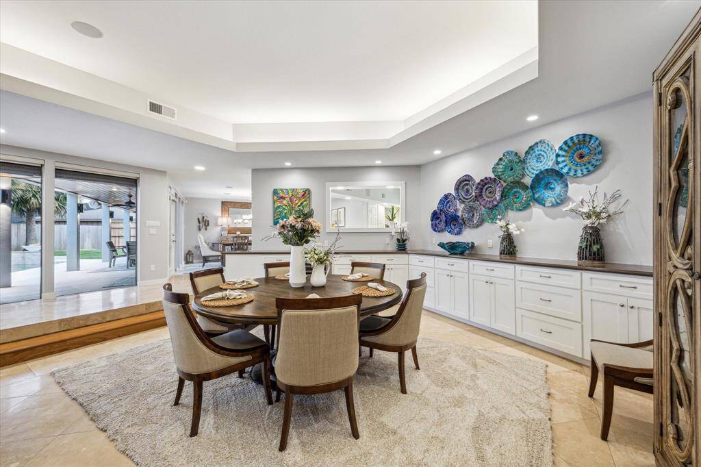 This spacious second dining area features a modern, open layout with elegant recessed lighting and a unique artistic wall display (does not convey). It includes a round table with stylish chairs on a plush rug. Large sliding glass doors lead to an outdoor space, enhancing natural light and connectivity.
