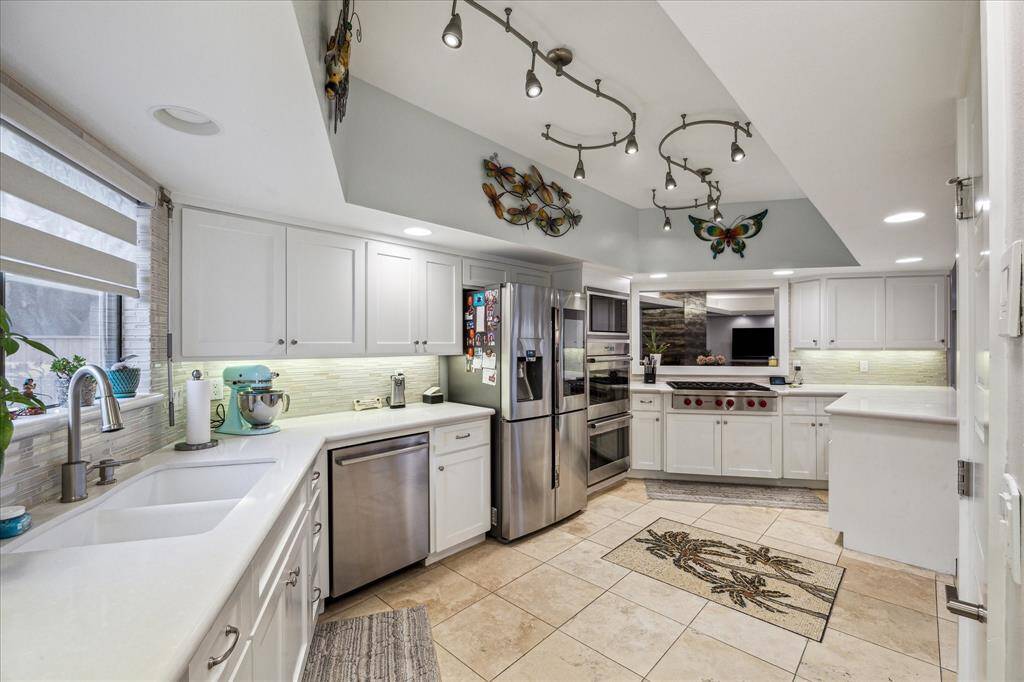 Another view of the kitchen features highend appliances, sleek white cabinetry, and ample counter space. It includes a double sink, tile flooring, and decorative lighting.