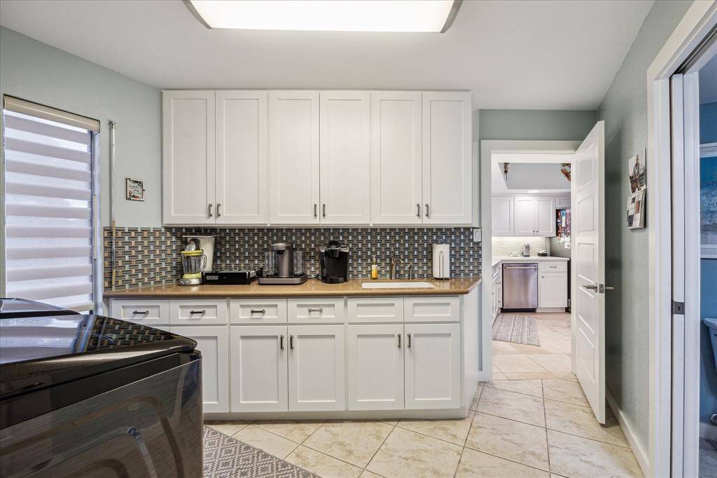 The indoor utility room has plenty of counter space, a built-in sink, and easy access to the kitchen. The neutral tile flooring complements the clean, contemporary design.