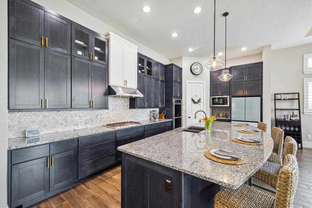 This stunning kitchen offers upgraded cabinetry with modern pulls and some glass-front uppers, sleek granite countertops, designer tile backsplash, stainless steel appliances, and a large walk-in pantry.