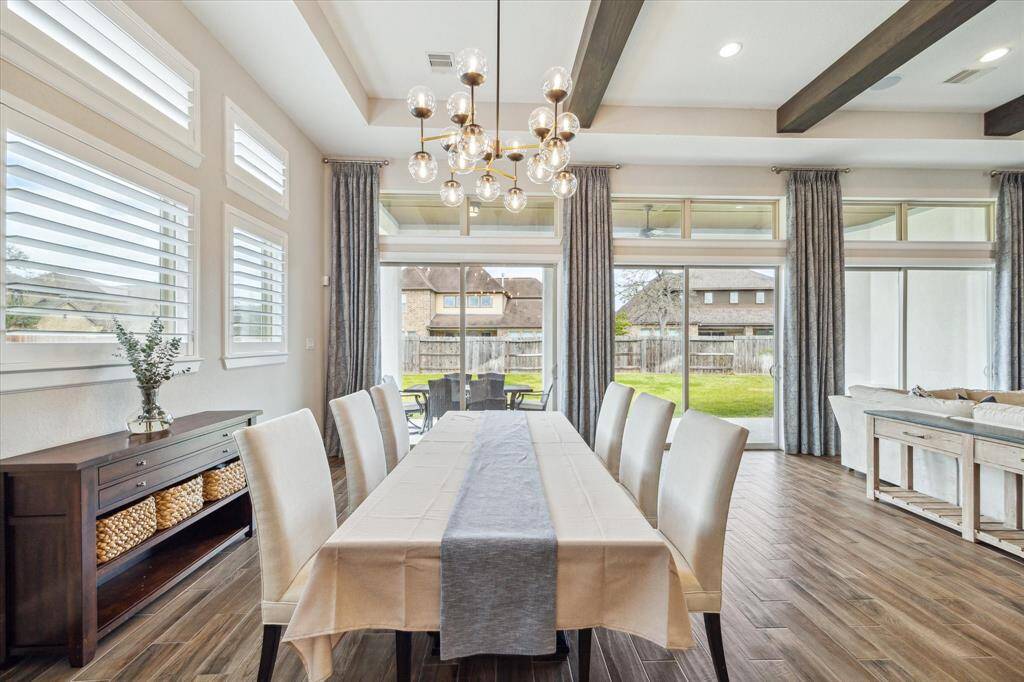 This elegant dining room provides the perfect backdrop for celebrating special occasions or enjoying romantic candlelit dinners. With chic lighting, rich wood-look tile flooring, and large windows that invite in natural light, this space effortlessly combines sophistication and warmth.