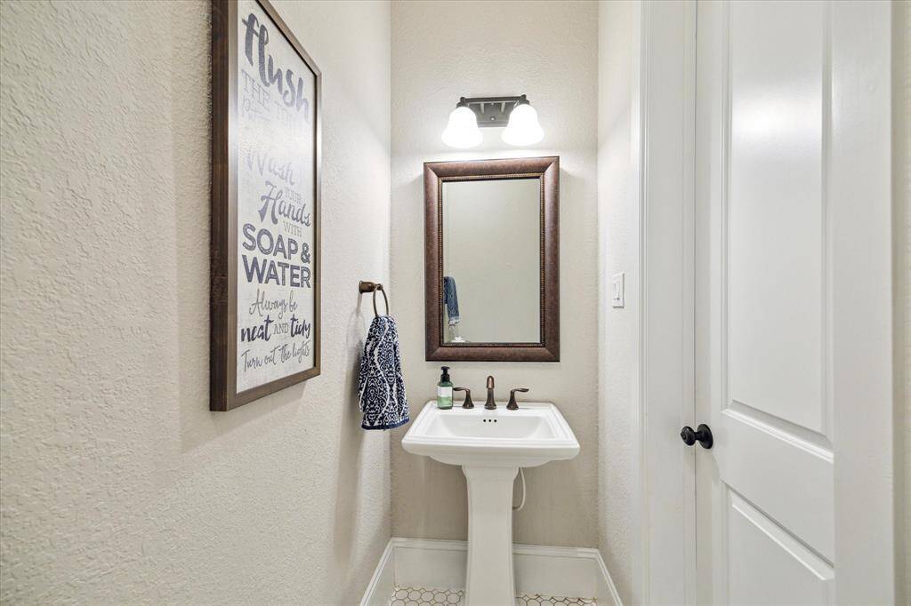 Located on the first floor near the stairs, the powder bathroom is convenient for guests. It features stylish tile flooring, neutral paint and a pedestal sink with a framed mirror and vanity lights above.