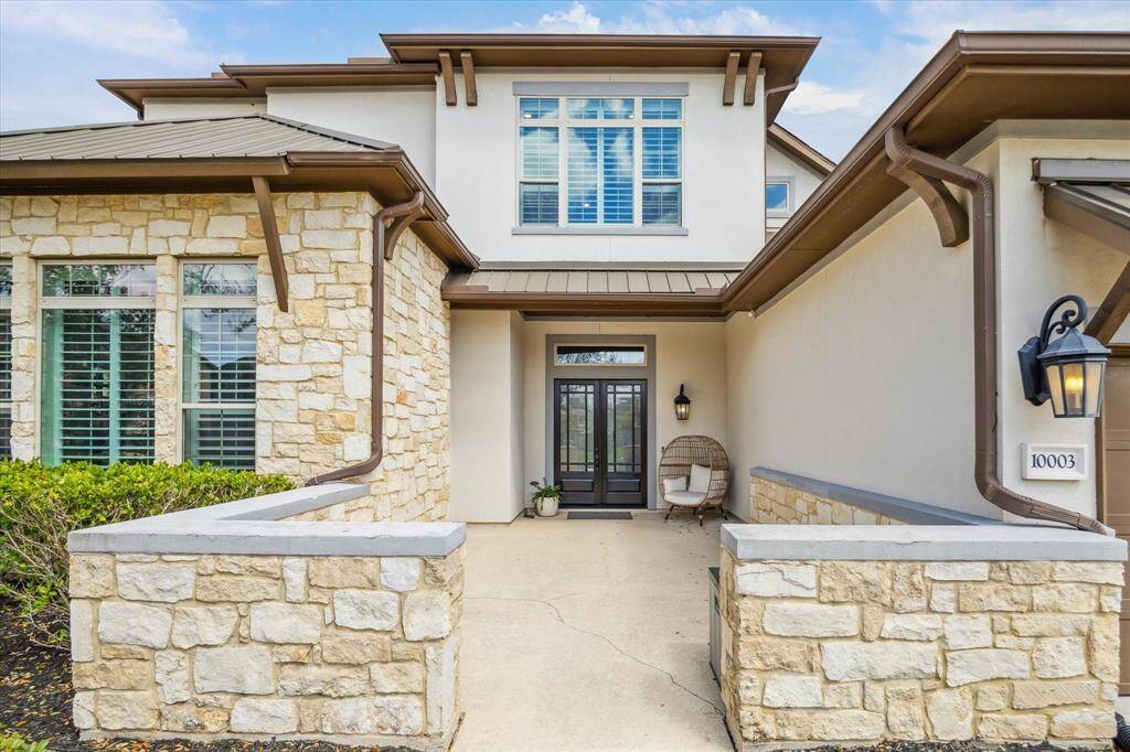 This inviting courtyard entry offers a warm welcome with its elegant stone accents, stucco finish, and stylish coach lighting. A perfect blend of charm and privacy, it leads to stunning double doors that set the tone for the exceptional home inside.