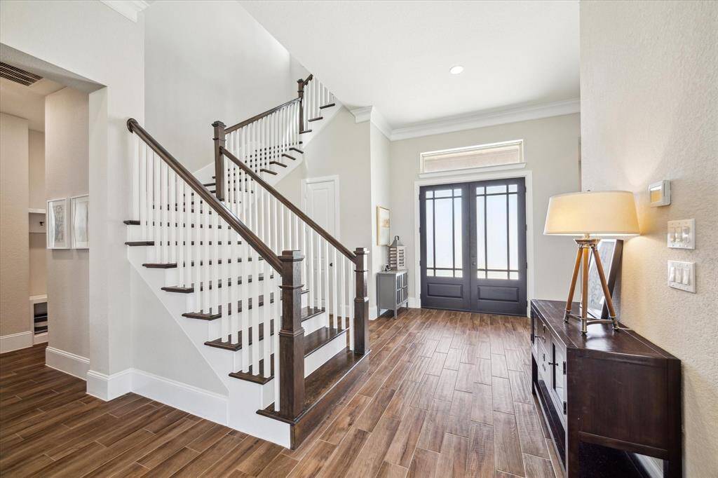 This impressive foyer offers an inviting welcome with wood-look tile flooring and 12' ceilings, neutral paint, thick crown molding, and a rich wood staircase.