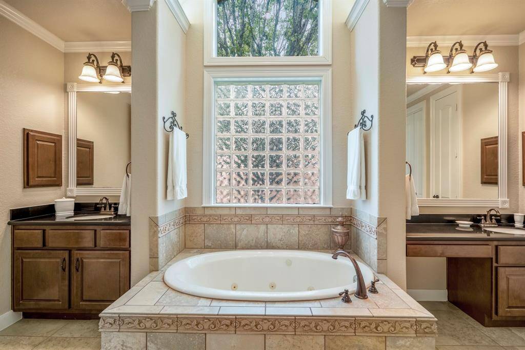 The en-suite bathroom offers a whirlpool tub under the stars, with glass block window offering a privacy window and the upper window allowing for nature to be seen and appreciated.  Dual sinks flank the tub area.
