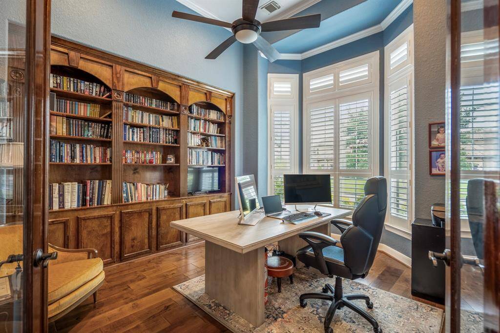 French glass doors framed by a wooden surround lead into a large study with custom wood bookshelves. plantation shutters and crown moldings.