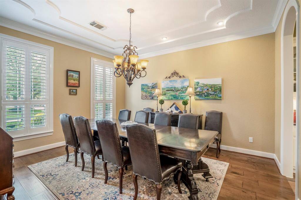 A timeless classic elegant formal dining room offers large windows that have plantation shutters, a tray scroll ceiling, wrought iron chandelier and crown moldings.