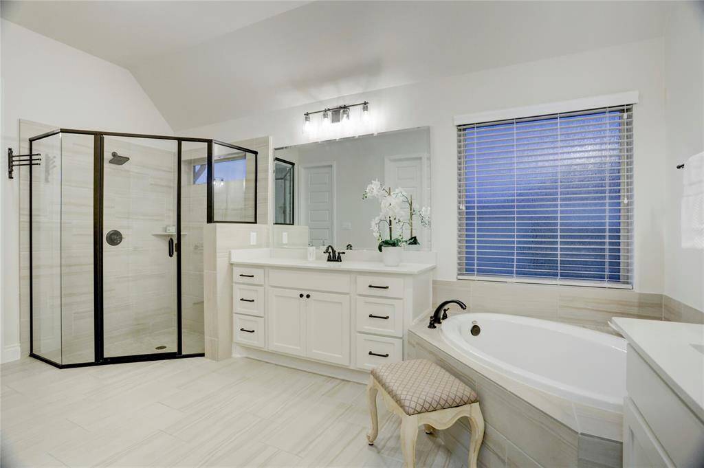 This thoughtfully designed bathroom combines beauty and practicality with ample cabinet space, elegant tile flooring, and a private soaking tub under a softly filtered window. The space is bright, calming, and truly rejuvenating.