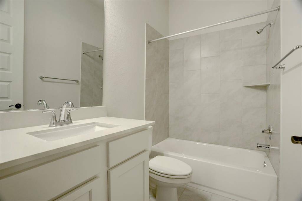 This private en-suite bathroom features a sleek tub/shower combination with modern tile surround—perfect for relaxing soaks or quick showers. Clean lines, a large mirror, and a contemporary vanity offer a fresh, functional design.