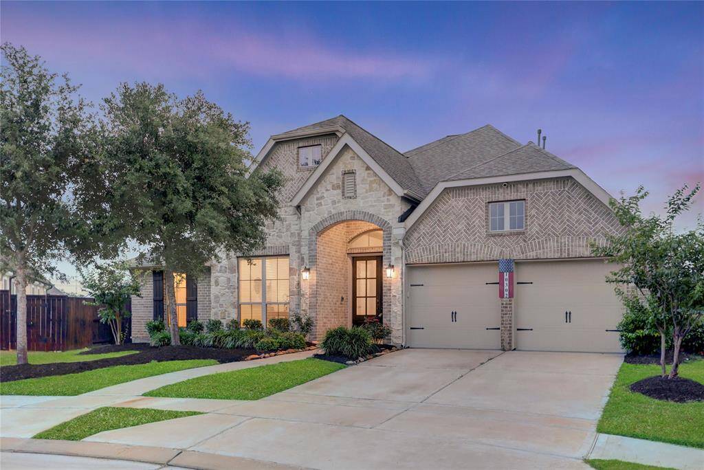 Charming front walkway lined with vibrant landscaping leads to a welcoming covered entry with double glass-panel doors and warm lighting—creating an inviting first impression.