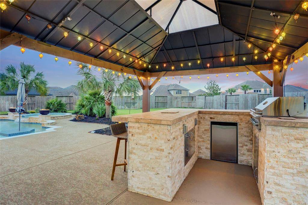 Fire up the grill under the custom gazebo, beautifully finished with stone counters and cafe-style lighting that sets the tone for festive evenings. Complete with a built-in grill, fridge, and bar seating, this is the go-to spot for serving drinks and catching up with friends.