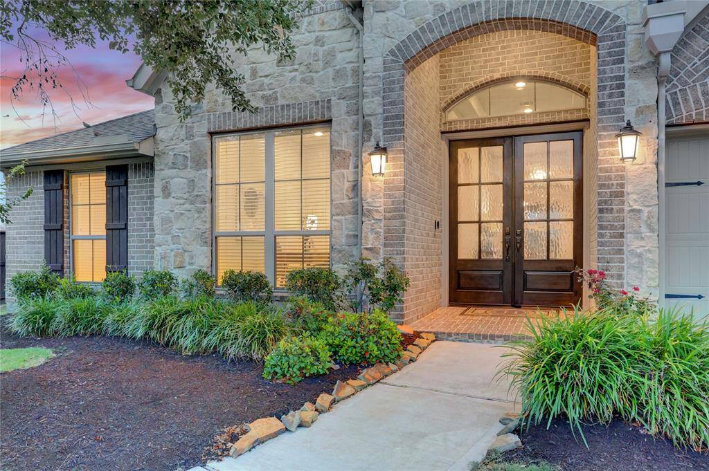 Inviting front elevation with rich stone and brick details, dual 8' glass-panel doors, and a charming covered entry. Beautifully landscaped for maximum curb appeal.