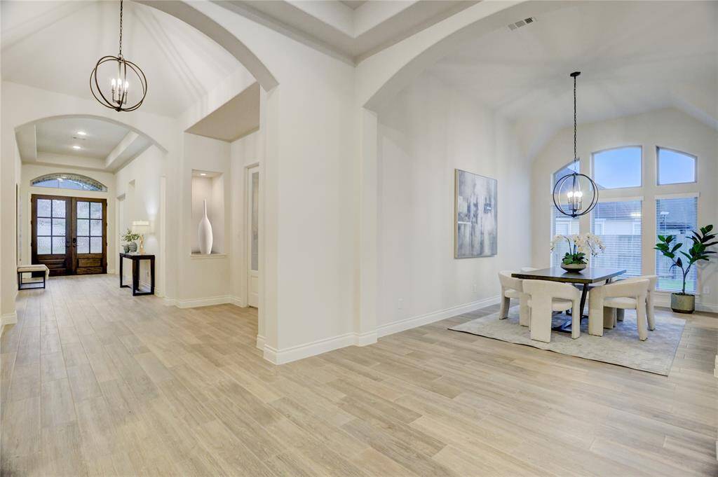 Light and bright grand hallway with high ceilings, designer light fixtures, arched entryways, and wood-look tile floors throughout. The formal dining room features soaring windows, elegant lighting, and an open flow perfect for entertaining.
