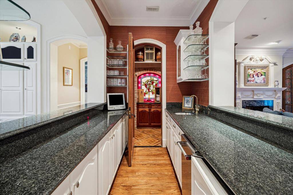 The double-sided bar, which opens to both the formal living room and family room, features elegant marble countertops and glass shelves. It includes a temperature-controlled wine room with a custom wrought iron door adorned with a grape leaf design and custom wood shelves for your wine collection. A cast stone arched niche with a custom backlit stained glass grape scene adds a touch of artistry and sophistication.