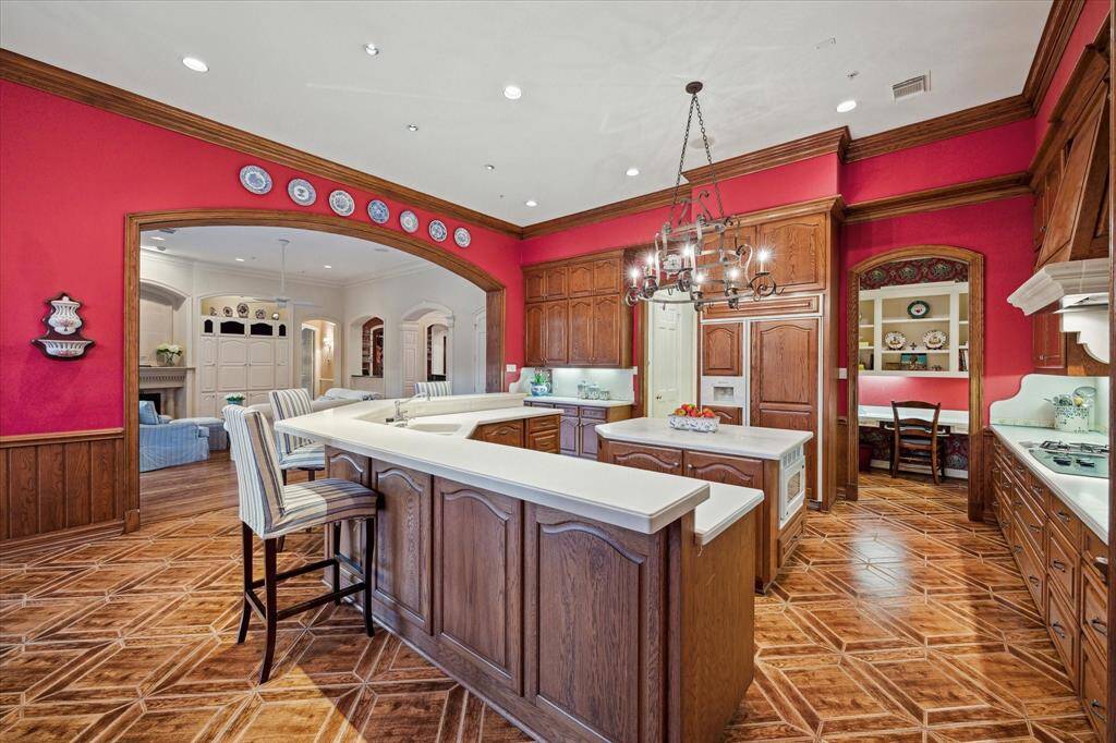 Another view of the kitchen showcases the extensive bar countertops, providing ample space for additional seating. The wood-paneled refrigerator and the spacious walk-in pantry offer abundant storage. Additionally, a charming home office features Brunswig & Fils wallpaper, built-in cabinets to hold printers and important papers, ensuring everyone stays organized for daily life. The kitchen's design is further elevated by luxurious touches, creating an inviting and sophisticated atmosphere.