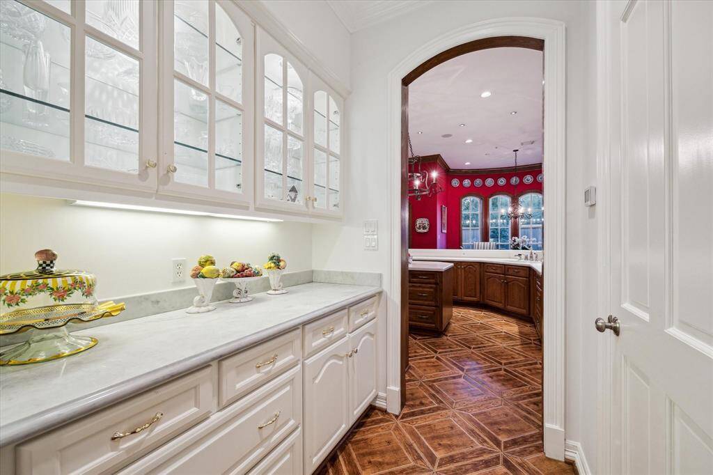 The butler's pantry boasts exquisite Carrera marble countertops, elegant under-cabinet lighting, and sophisticated interior rope lighting that illuminates the glass shelves.