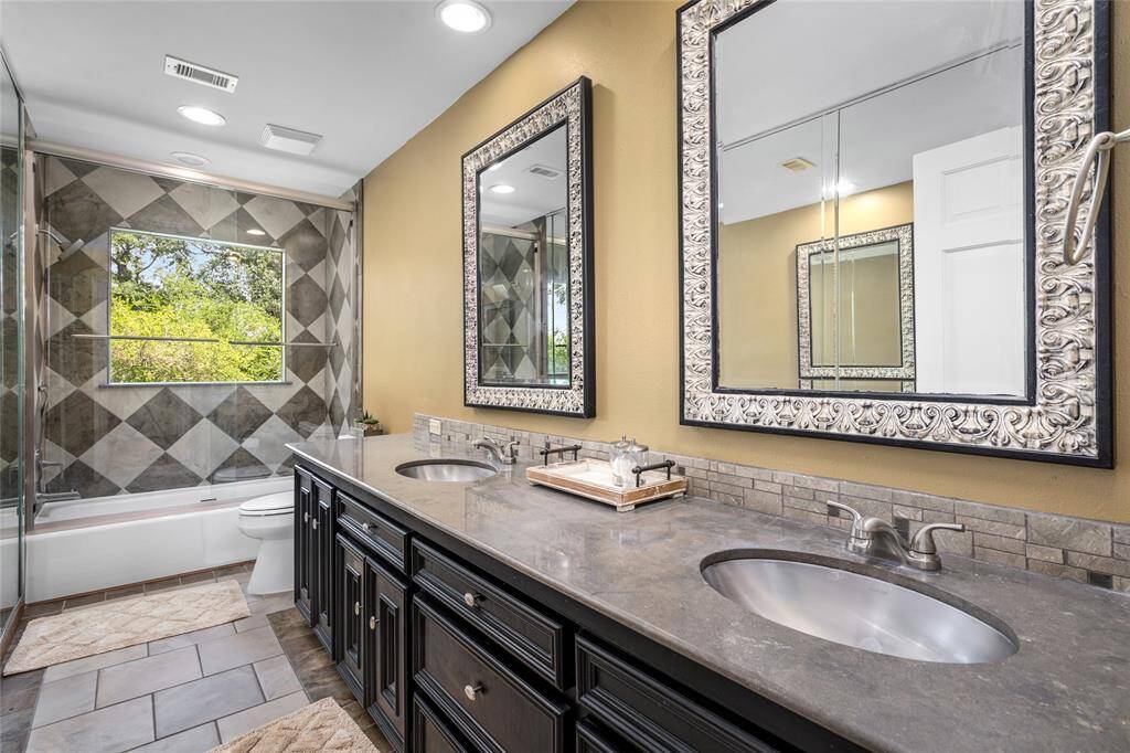 Updated secondary bathroom featuring a full-wall mirror, brand new glass shower door, and resurfaced tub. The dual vanity offers ample space, combining modern style with functionality for everyday use.