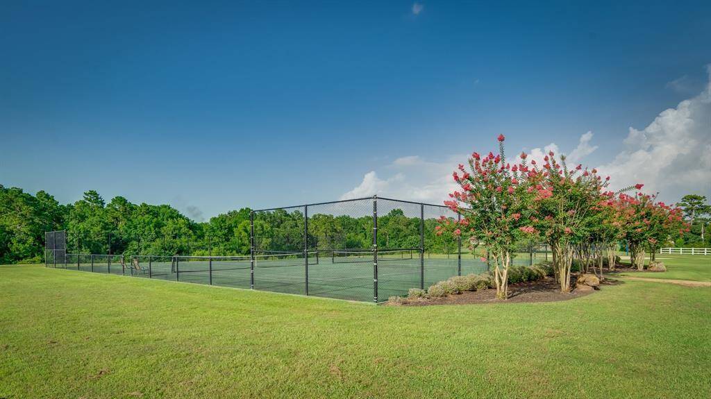 This is a well-maintained community tennis court surrounded by lush greenery and vibrant flowering shrubs, offering a great recreational space within a peaceful environment.