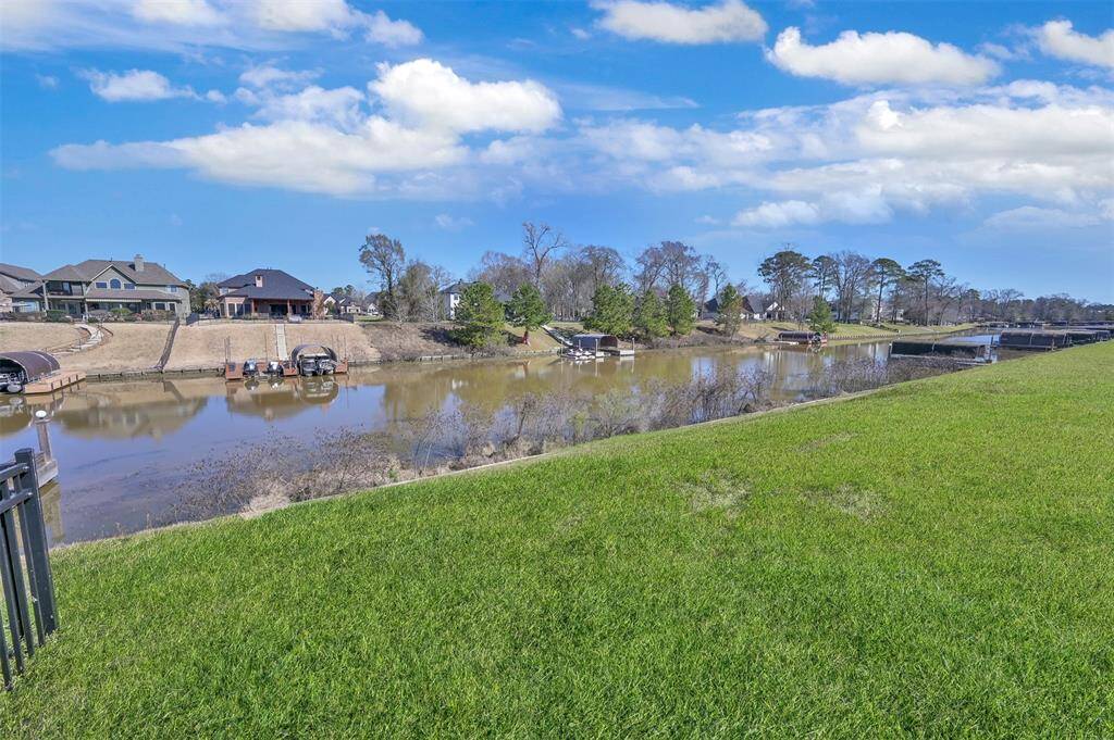 This photo shows a waterfront property with a lush green lawn leading to a calm body of water, where private docks are visible. The neighborhood features spacious homes with generous yards, and a bridge in the distance connects the community.