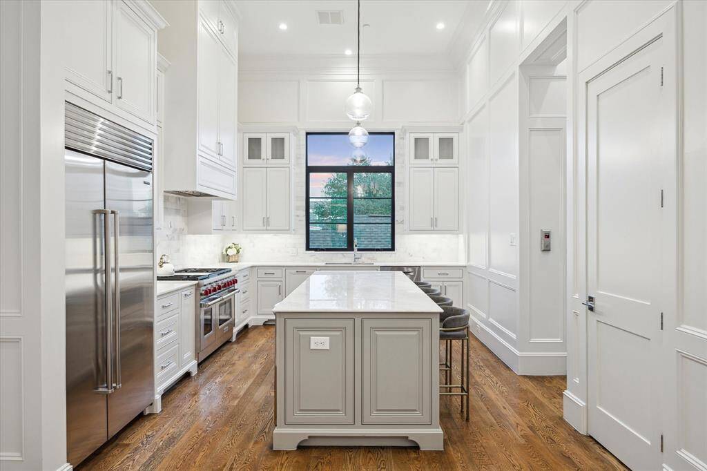 This luxurious kitchen features high ceilings with recessed lighting and elegant pendant lights hanging over a large central island.