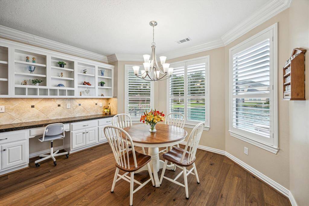 The breakfast room not only offers stunning lake views but also features a chandelier and a wall of custom cabinetry, including open shelving and a built-in desk area with full extension printer shelf and under counter electrical plug.