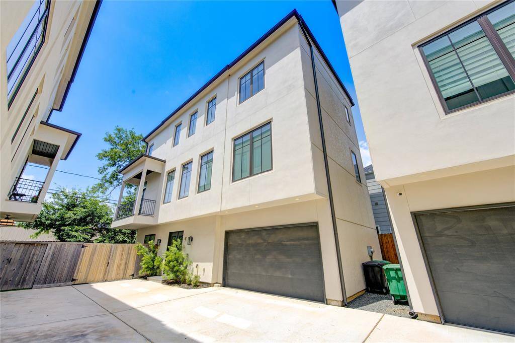 This modern three-story townhouse features a sleek exterior with large windows for natural light. It includes an attached garage, a small balcony, and is set in a cozy, fenced area, providing privacy and security.