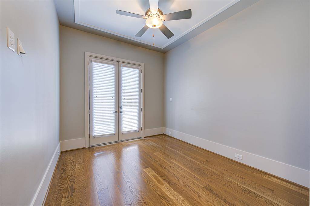 This room features hardwood floors, neutral walls, a ceiling fan, and French doors with blinds, creating a bright and airy space.