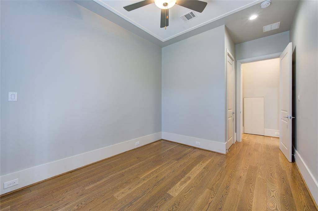 This is a bright room with hardwood floors, neutral walls, and a ceiling fan. It features recessed lighting and a doorway leading to another area, offering a clean and modern space.