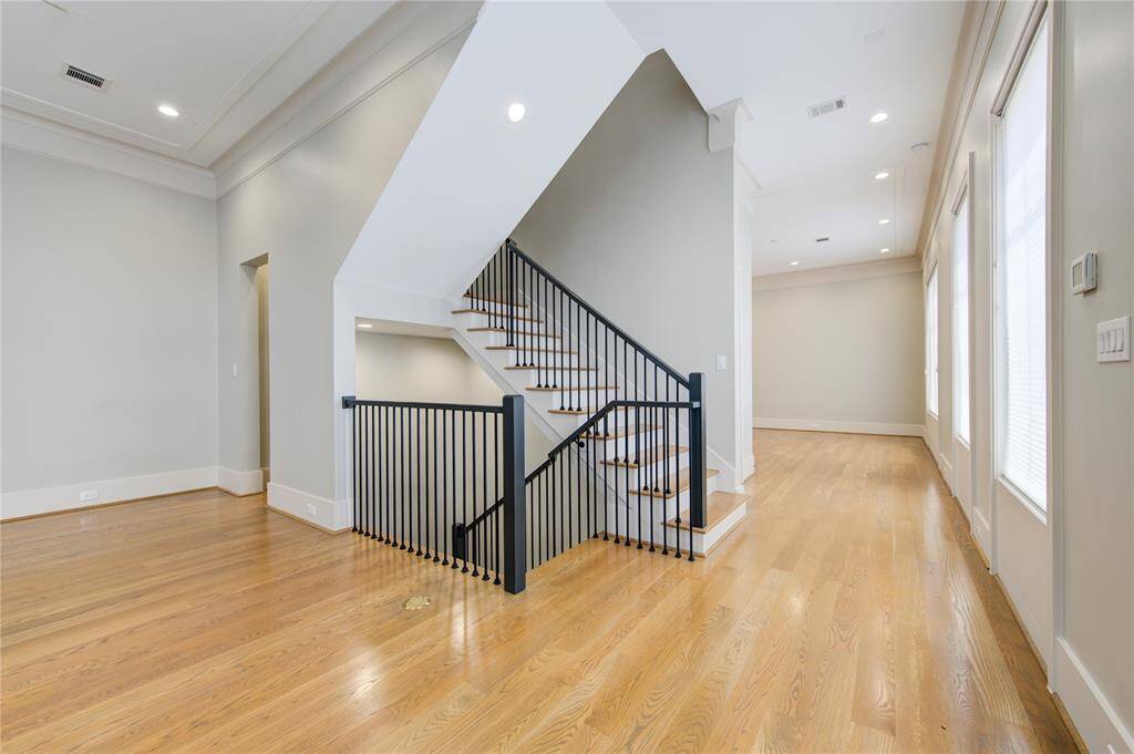 This spacious area features an elegant staircase with modern black railings, hardwood floors, and ample natural light from large windows, creating a bright and inviting atmosphere.