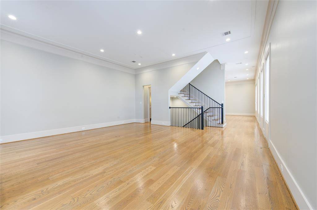 This spacious room features beautiful hardwood flooring, a modern staircase with sleek black railings, and abundant natural light from large windows. Ideal for an open-concept living area.