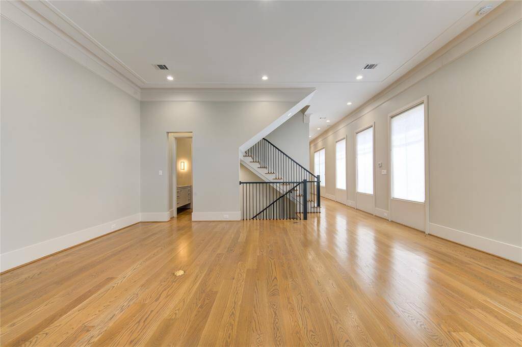 This spacious room features polished hardwood floors, a modern staircase with black railings, and abundant natural light from large windows, creating a bright and inviting atmosphere.