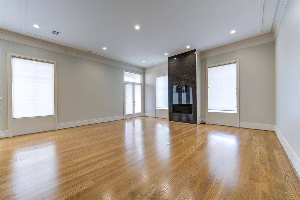 Spacious living room with hardwood floors, large windows, recessed lighting, and a sleek black fireplace.
