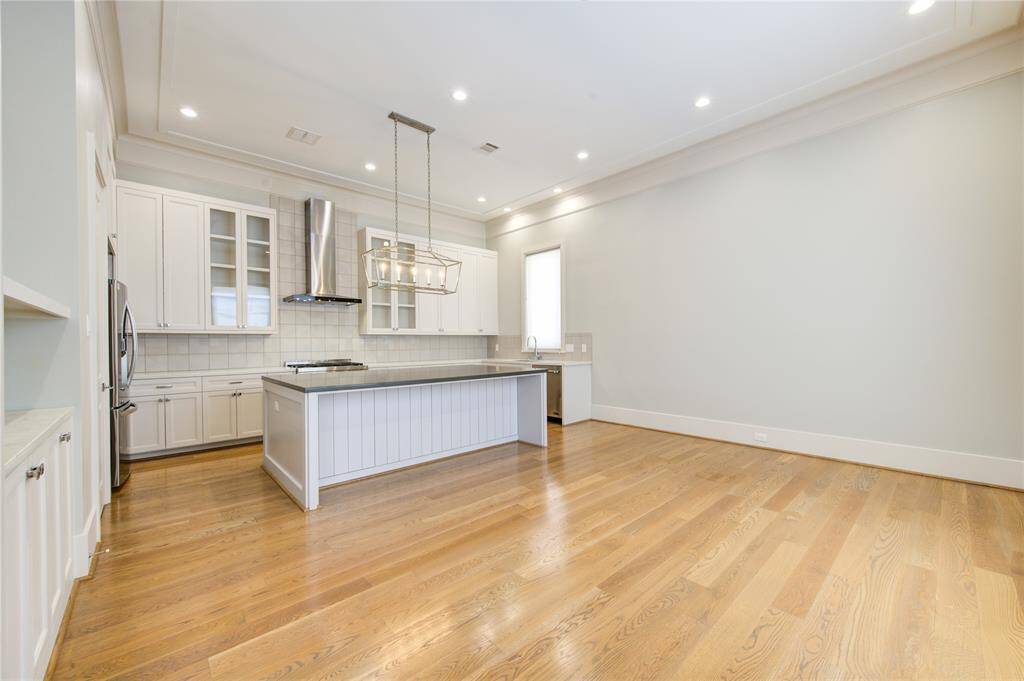 This photo showcases a spacious, modern kitchen with an open layout. It features light wood floors, white cabinetry, a large island, and stainless steel appliances, creating a bright and inviting atmosphere.