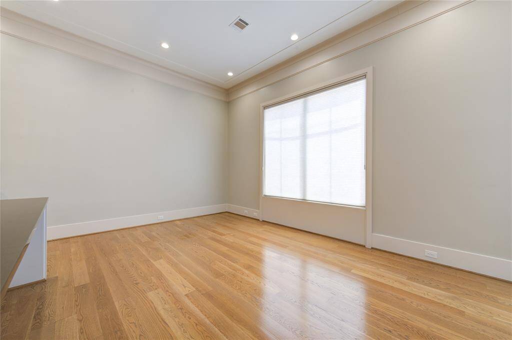This room features hardwood flooring, neutral walls, and a large window with blinds, providing ample natural light. Recessed lighting and high ceilings add to the spacious feel, making it versatile for various uses.