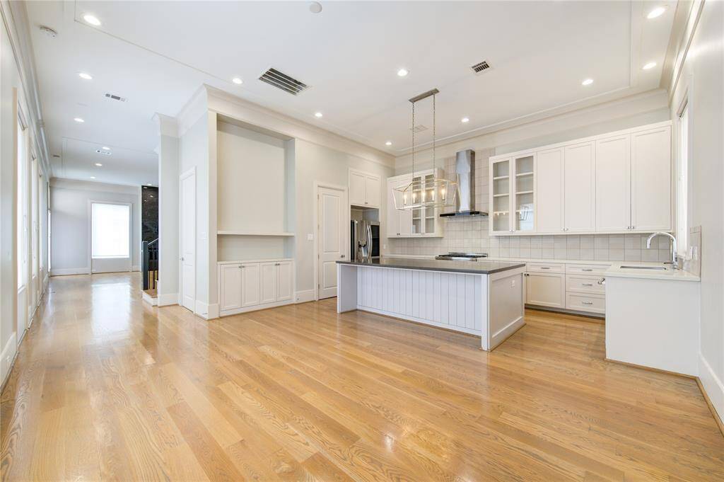 This photo showcases a spacious, open-concept kitchen and living area with hardwood floors. The modern kitchen features a large island, stainless steel appliances, and ample cabinetry. High ceilings and recessed lighting add to the bright and airy feel of the space.