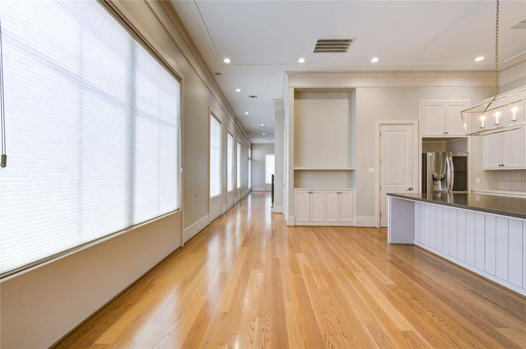 This photo showcases a bright, open-concept space with hardwood floors, large windows with blinds, and a modern kitchen area featuring a stainless steel refrigerator and an island with pendant lighting.