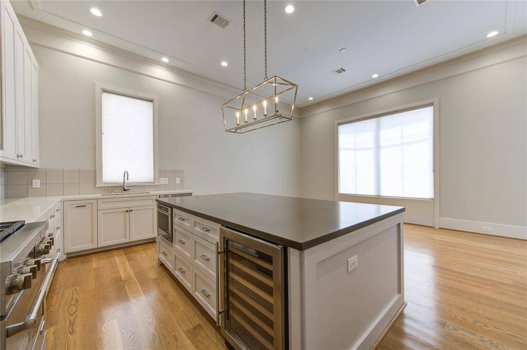 This spacious kitchen features hardwood floors, a large island with built-in storage, and a modern light fixture. It also includes stainless steel appliances, ample cabinetry, and large windows for natural light.