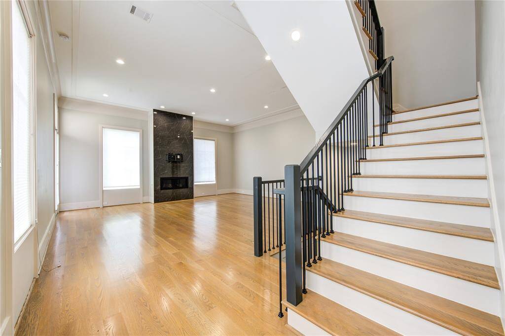 This spacious living area features beautiful hardwood floors, a modern fireplace, and a sleek staircase with black railings, creating a stylish and inviting atmosphere.