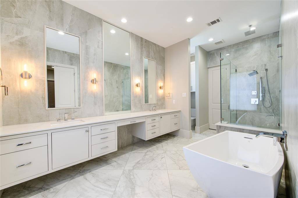 This luxurious bathroom features a sleek, modern design with a spacious dual vanity, large mirrors, elegant lighting, a glass-enclosed shower, and a freestanding bathtub. The neutral color palette and high-end finishes create a spa-like atmosphere.